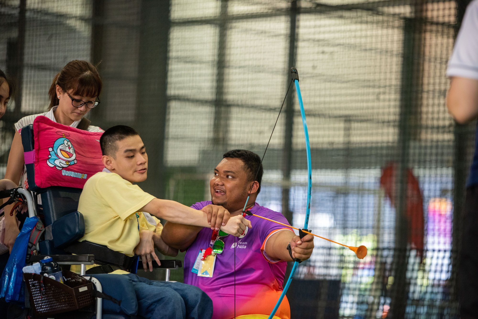Photo of participant in wheelchair trying out archery and being assisted by a volunteer