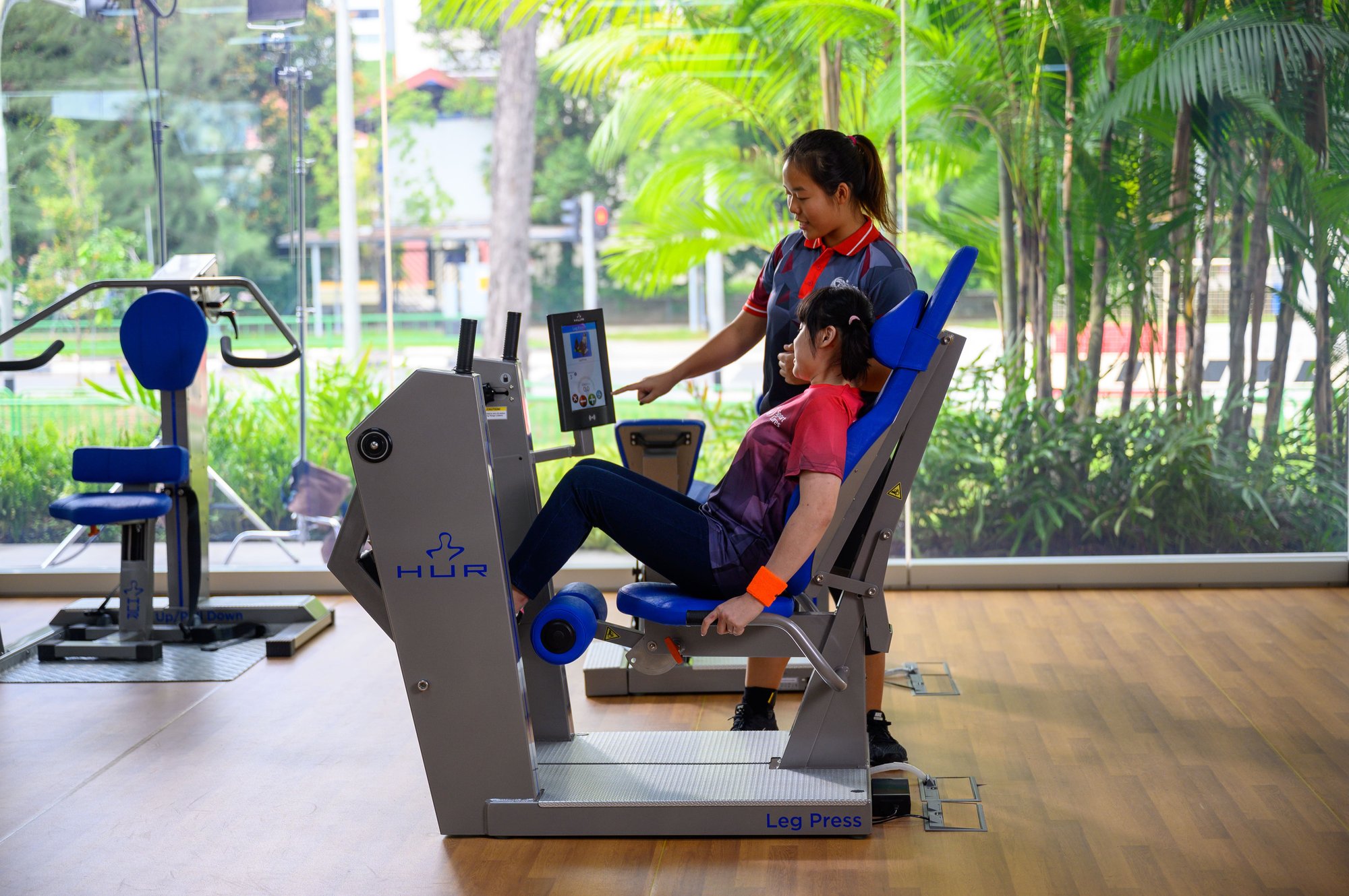 Photo of a female volunteer helping a female users with special needs to use a gym machine